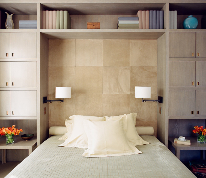 Bed with light gray velvet cover and white pillows inside wood bed niche with pair of sconces and surrounding cabinetry.