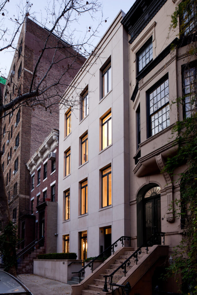 A modern townhouse with a limestone facade with a brick building in the rear and a brownstone in the foreground.