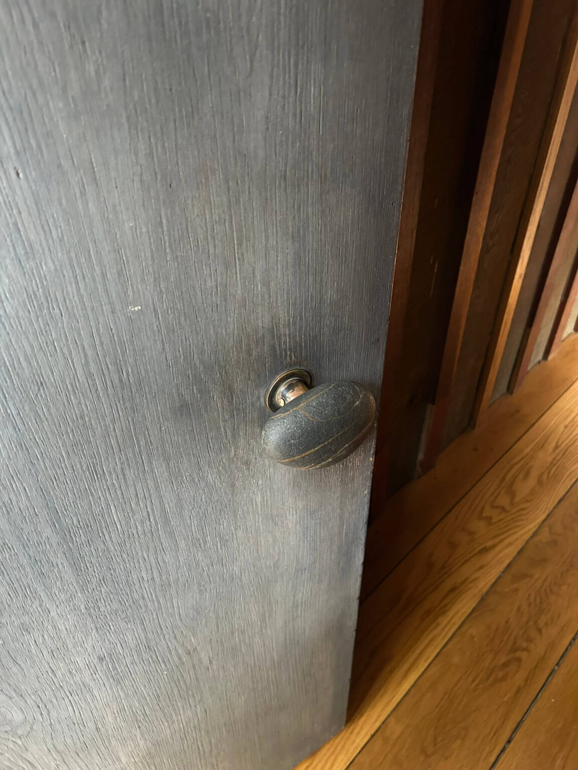 Close-up of a gray wood door with a smooth rock in dark gray stone as the doorknob.