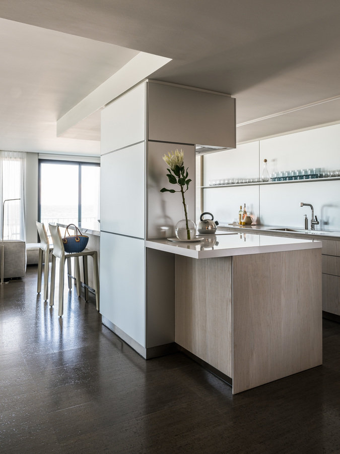 Open kitchen in white lacquer and white oak veneer and island with built-in range and range hood and counter with stools.