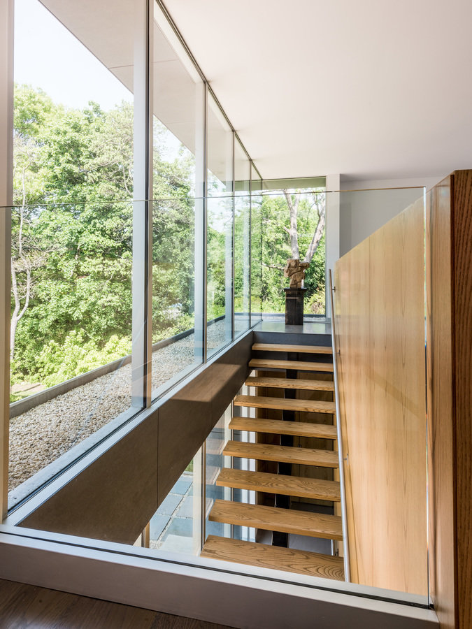 Upper-level staircase landing with floor-to-ceiling windows, open wood stair with railing on wood wall and a glass partition.