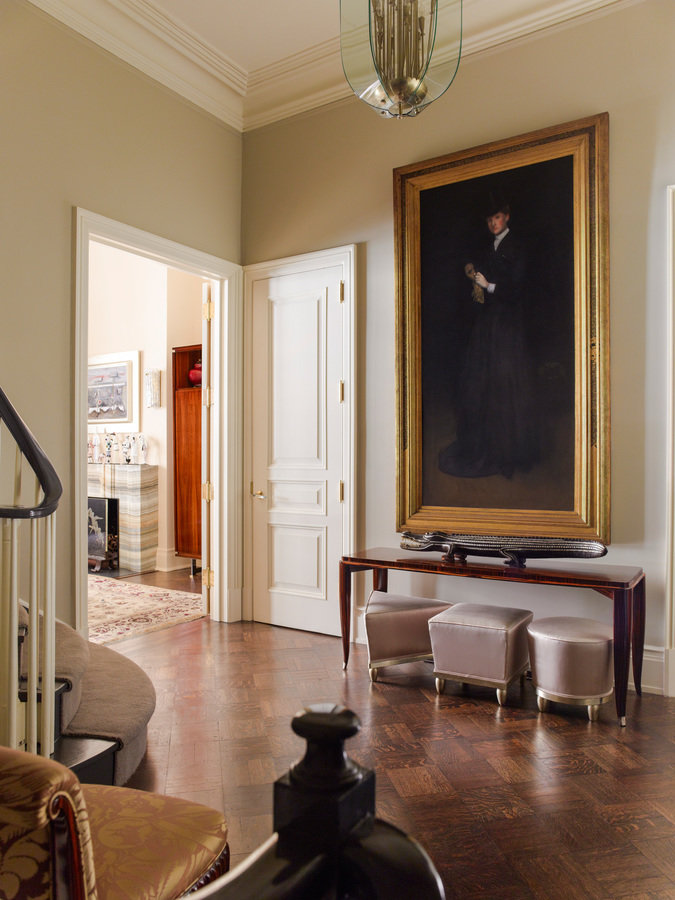 Foyer with dark parquet floors and neutral walls; large painting in a gold frame on facing wall, doorway into living room.