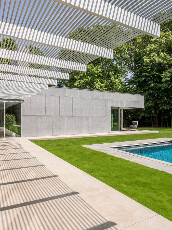 Rear patio with custom aluminum sunshade overhead, lawn with swimming pool; primary bedroom with outdoor area in background.