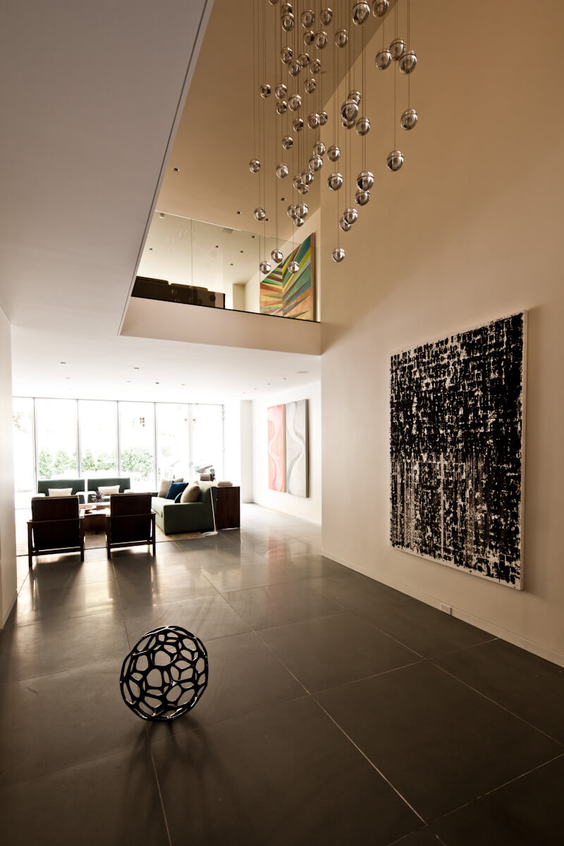Modern home with dark gray stone flooring, white walls with art, hanging glass spheres, and a sofa and chairs in background.