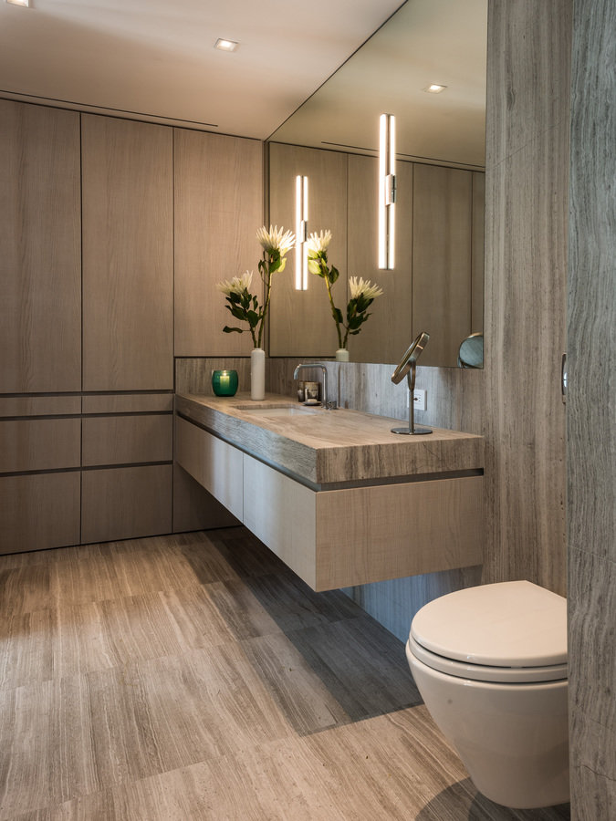 Modern bathroom with walls, floor and vanity counter in limestone, mirror, white oak veneer cabinetry and modern toilet.