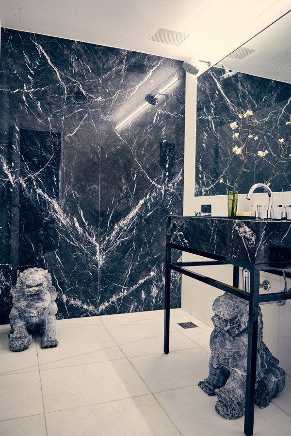 Bathroom with white stone floor, black marble shower and standing sink vanity, mirror and two Chinese stone lions.