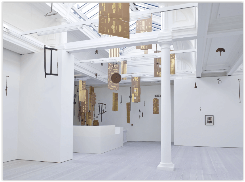 A white interior space with an empty floor, a column and a skylight with tan and gold banners suspended from the ceiling.