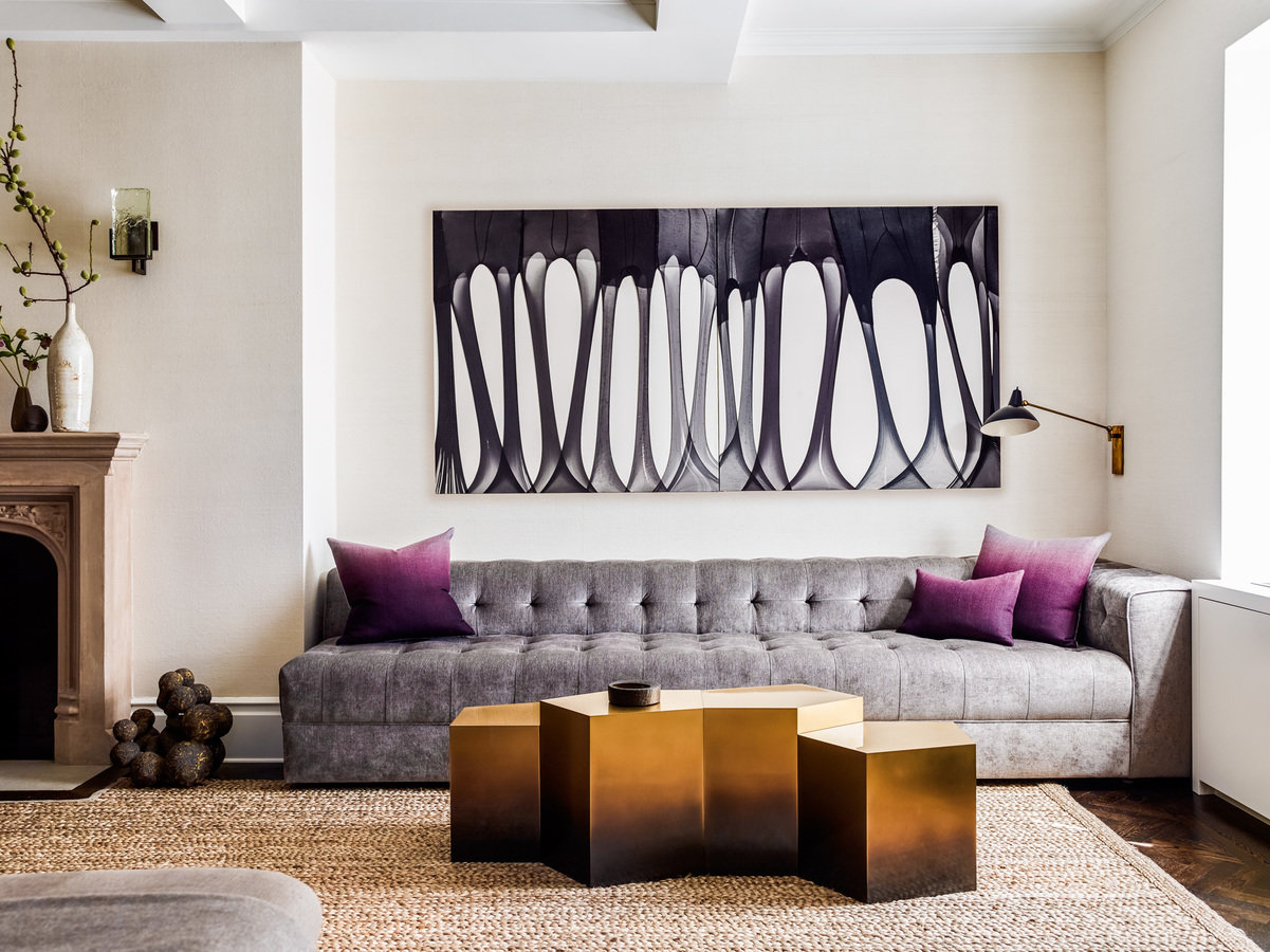 Large modern sofa with gray tufted upholstery against beige wall, black and white modern art, sculptural metal coffee table.