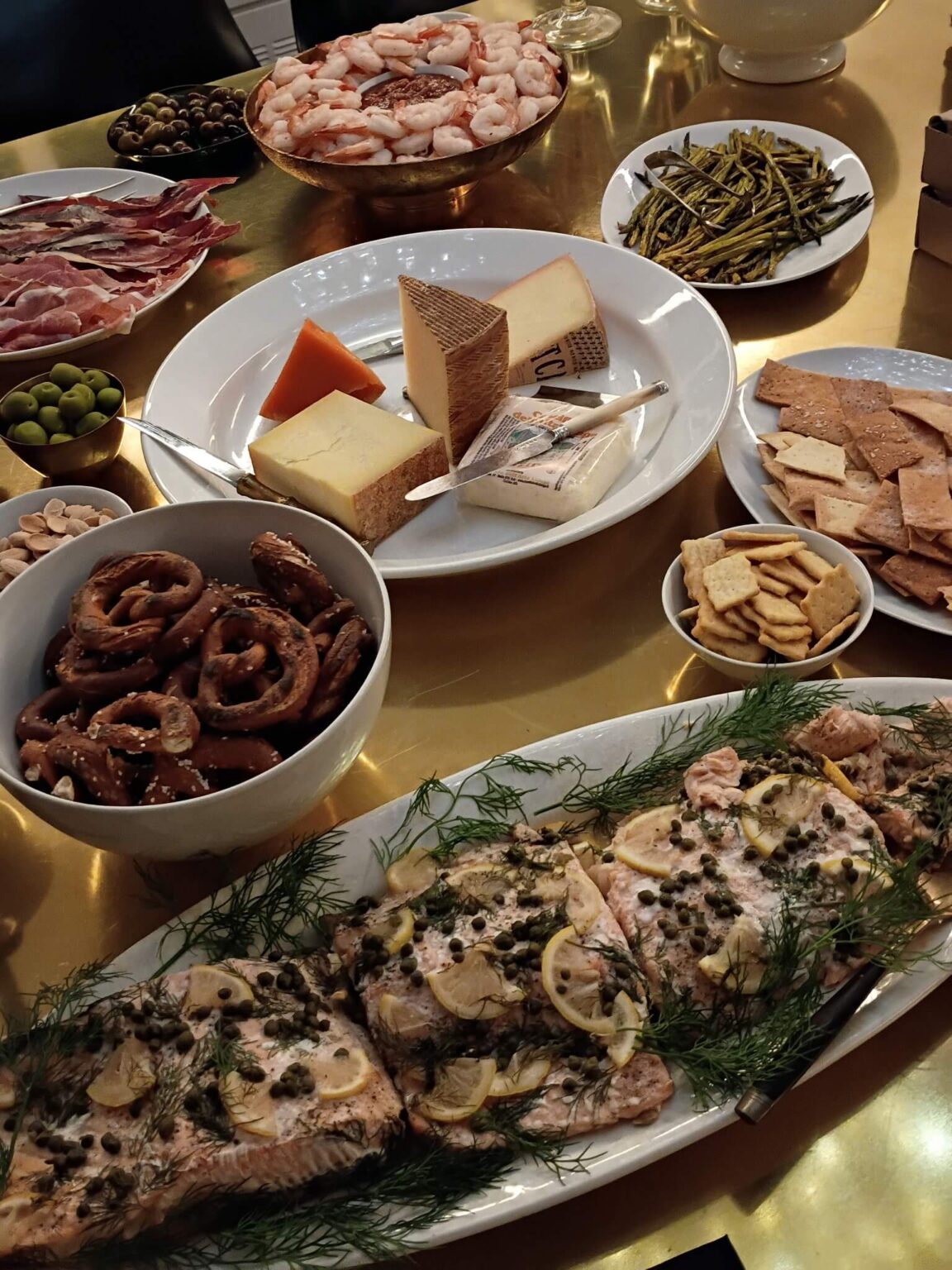 Brass dinner table with plattters of food including salmon, shrimp cocktail and cheese.
