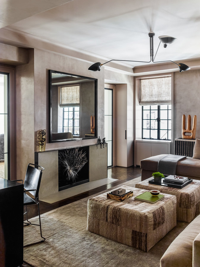 Modern den in a neutral palette with minimalist fireplace, a mirror over the mantel, silk rug and pair of oversized ottomans.