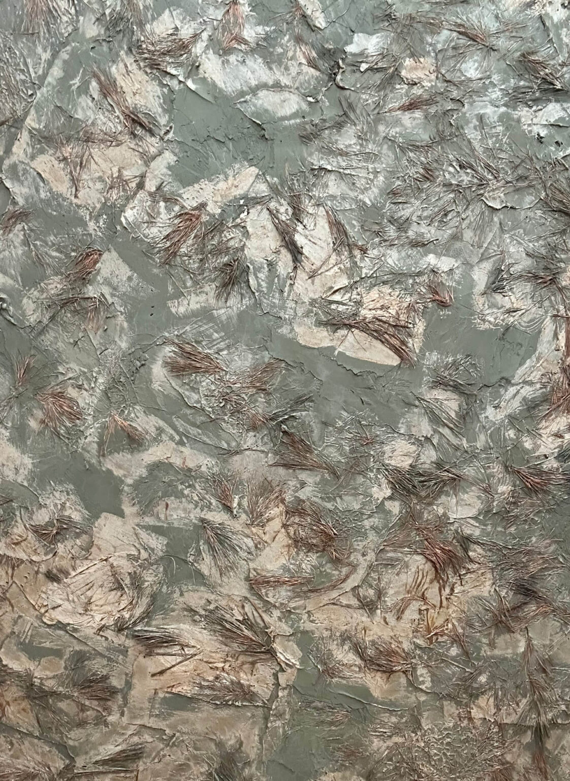 Close-up of a decorative wall finish in a light green-gray and beige plaster with dried pine needles embedded in the surface.