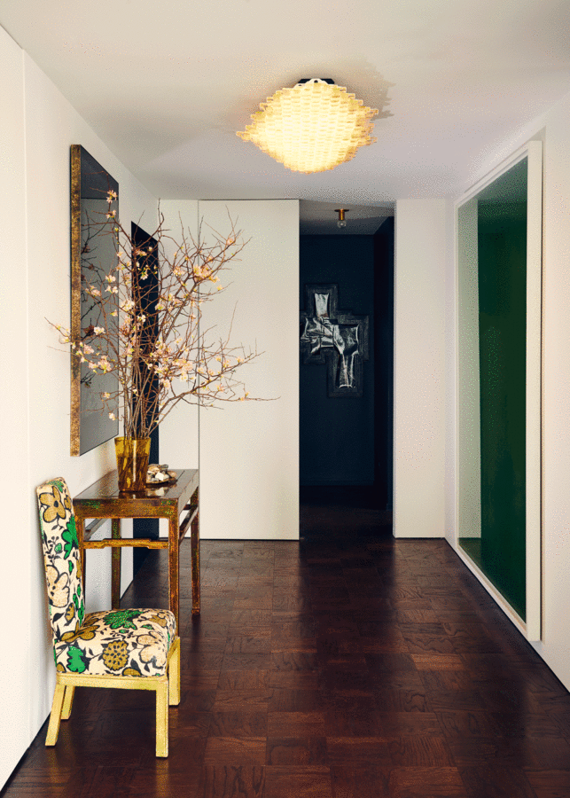 Foyer with decorative glass ceiling light, console table, vase of branches, vintage chair, black wall and art in background.