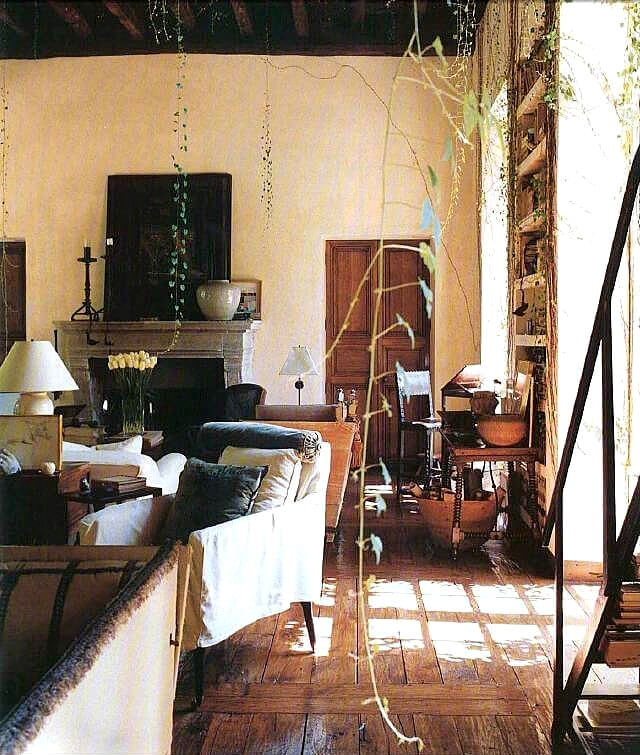 An interior with old wood floors, a dark wood beam ceiling with seating, lamps, tables and chairs and a fireplace at the rear.