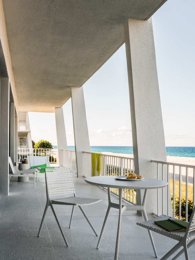 Modern white concrete balcony with white café table and chairs and view of the ocean.