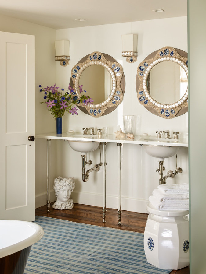 Bathroom with two-sink vanity stand, pair of round decorative mirrors, blue and purple flowers, blue and white striped rug.