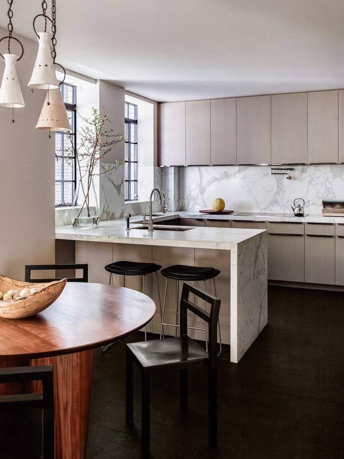 Modern kitchen with pale wood cabinetry, white marble counter and backsplash, black slate floor, round wood breakfast table.