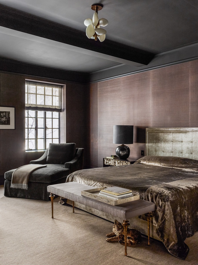 Bedroom in black, brown, and bronze palette, bed with upholstered headboard and velvet cover, spherical table lamp and bench.