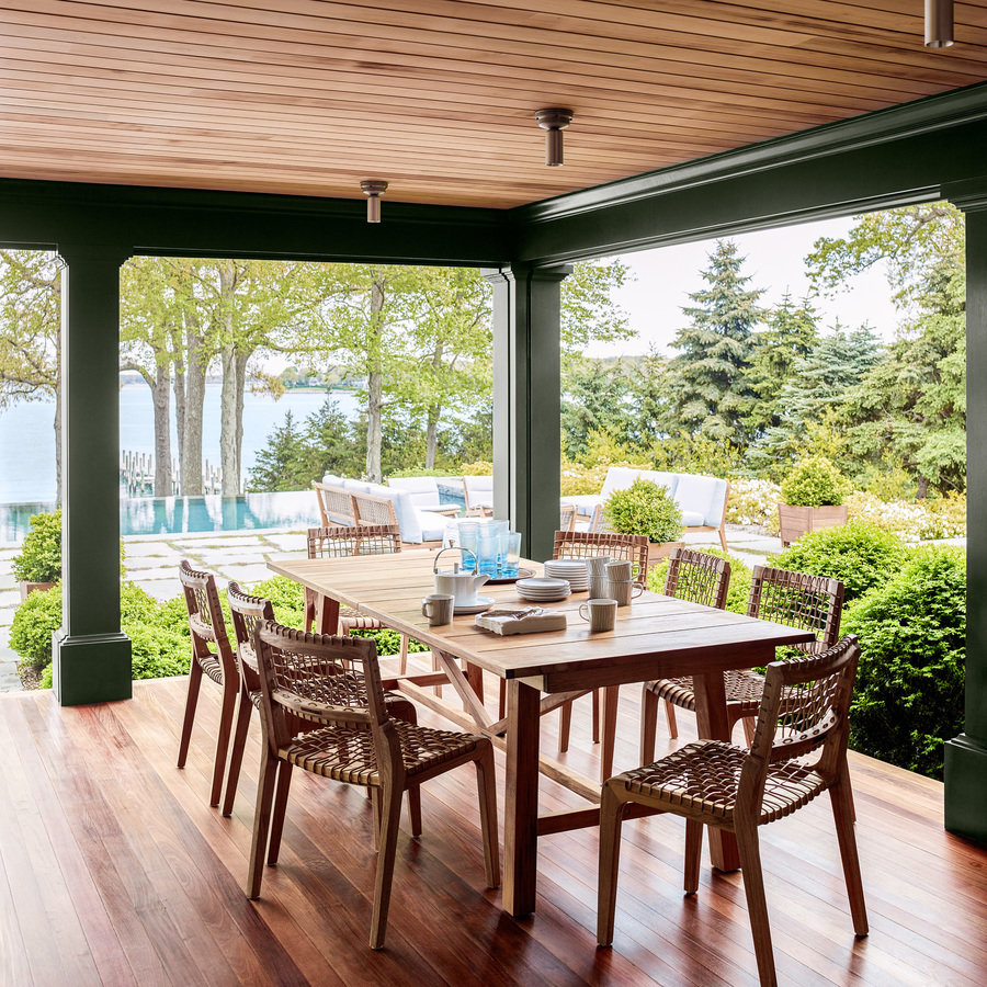 Wood dining table and chairs in rear porch with wood ceiling and wood floor and view to pool patio and bay in the distance.