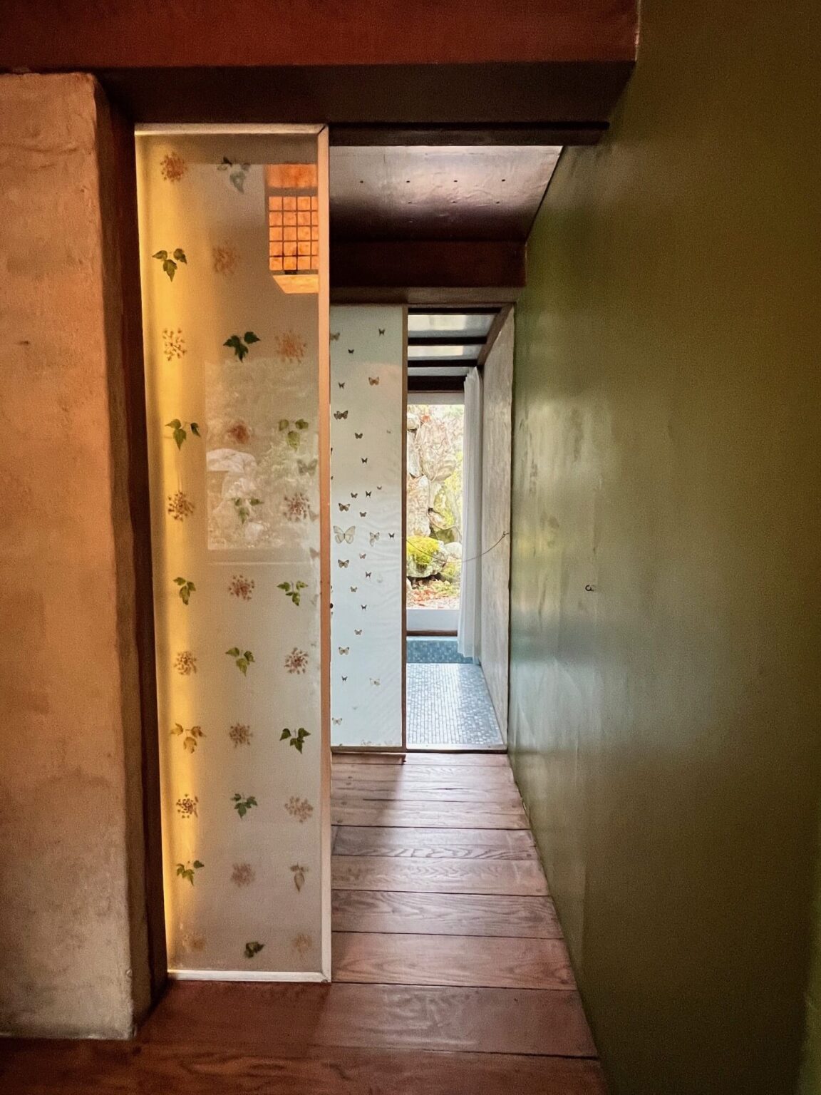 Corridor with an olive green wall at right, wood floor and translucent panels with pressed flowers and butterflies.