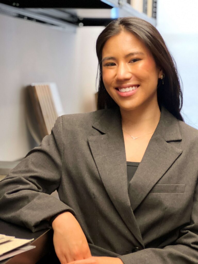 A dark-haired woman in a gray blazer posed, with her arm on a counter.