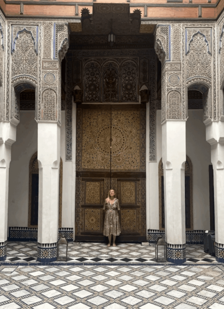 A woman standing inside a building with columns, ornate walls and ceiling and a patterned floor.