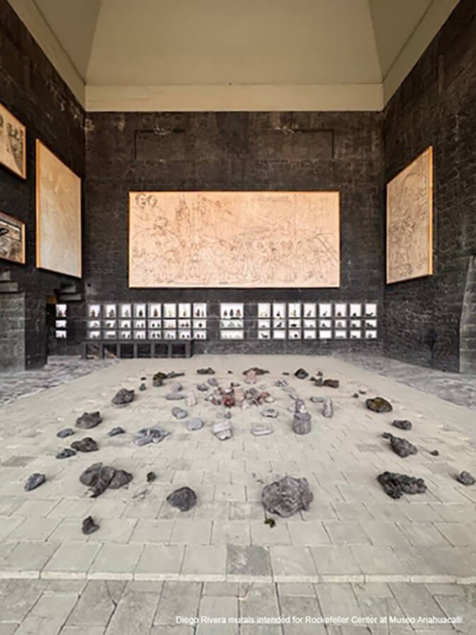 A large interior space with black stone walls and a light gray stone floor, with oversized, unfinished murals.