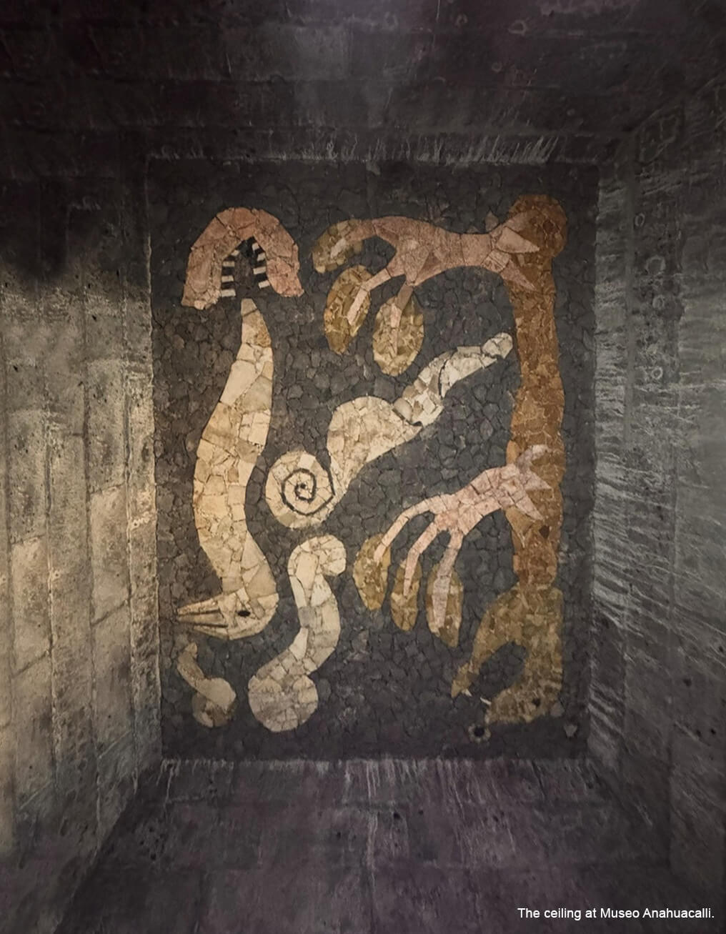 A dark gray, beige and gold colored stone mosaic mural on the ceiling of the Museo Anahuacalli.