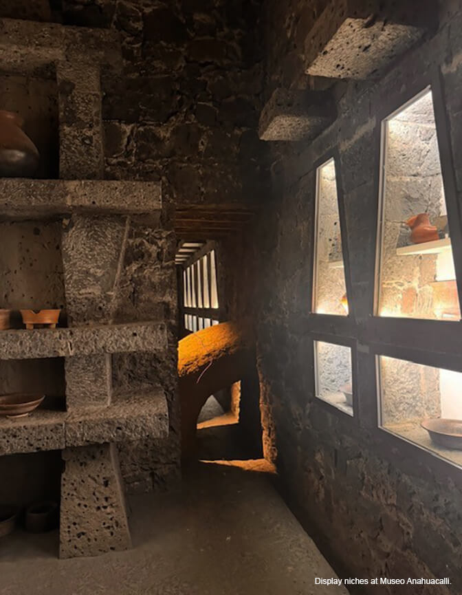 A stone interior with geometric shaped shelves and to the right, illuminated trapezoidal display niches for pottery.