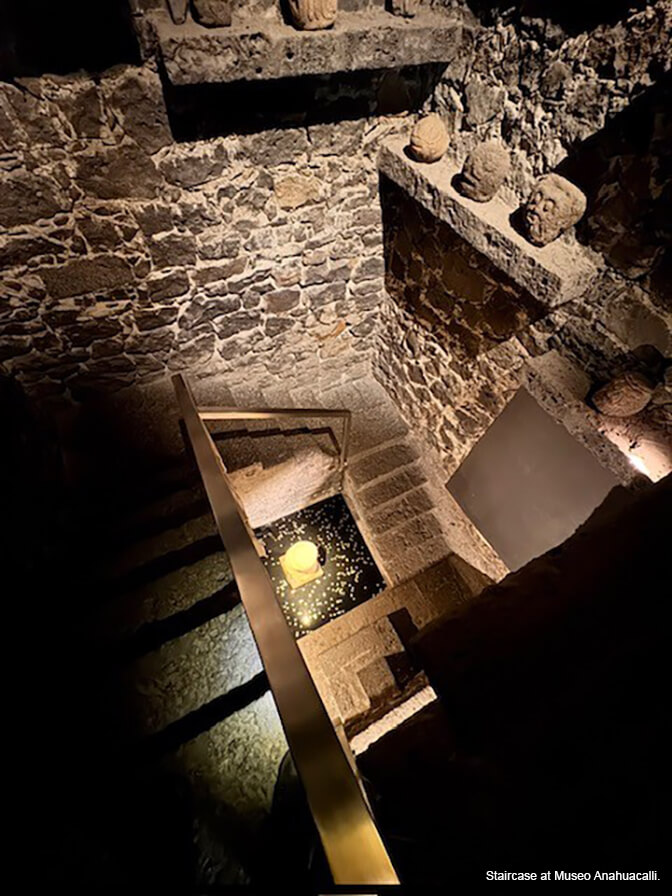 A stone interior with a stone staircase and stone shelves displaying carved sculptures.