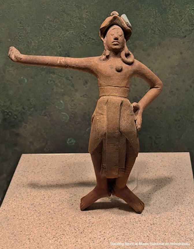 A brown clay tabletop sculpture of an ancient person standing with one hand on his hip and the other outstretched.