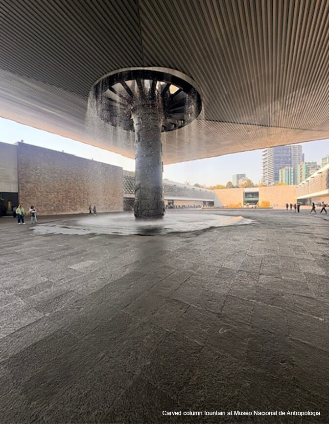 A large gray stone plaza with a flat roof and a large column fountain in the center.