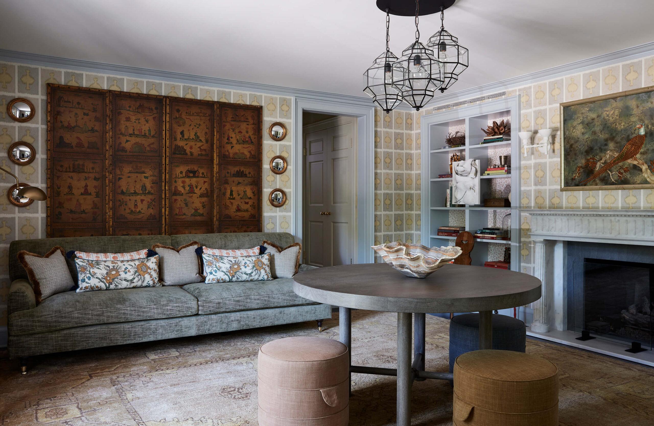 Sitting room with grid-pattern wallpaper, wood screen, sofa, round table with stools and trip of glass chandeliers.