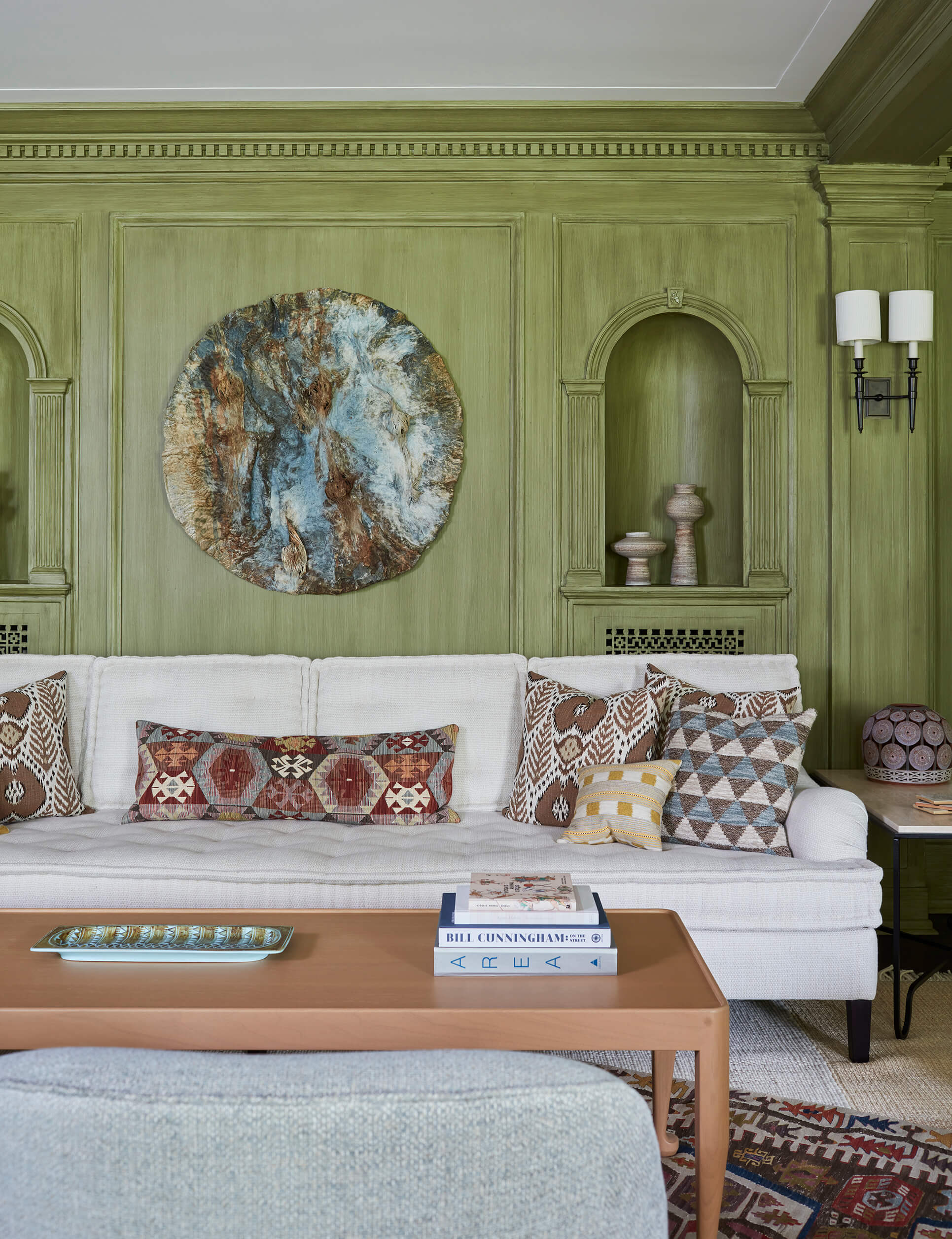 Living room with green-painted millwork walls, round artwork, white sofa with pillows and coffee table.