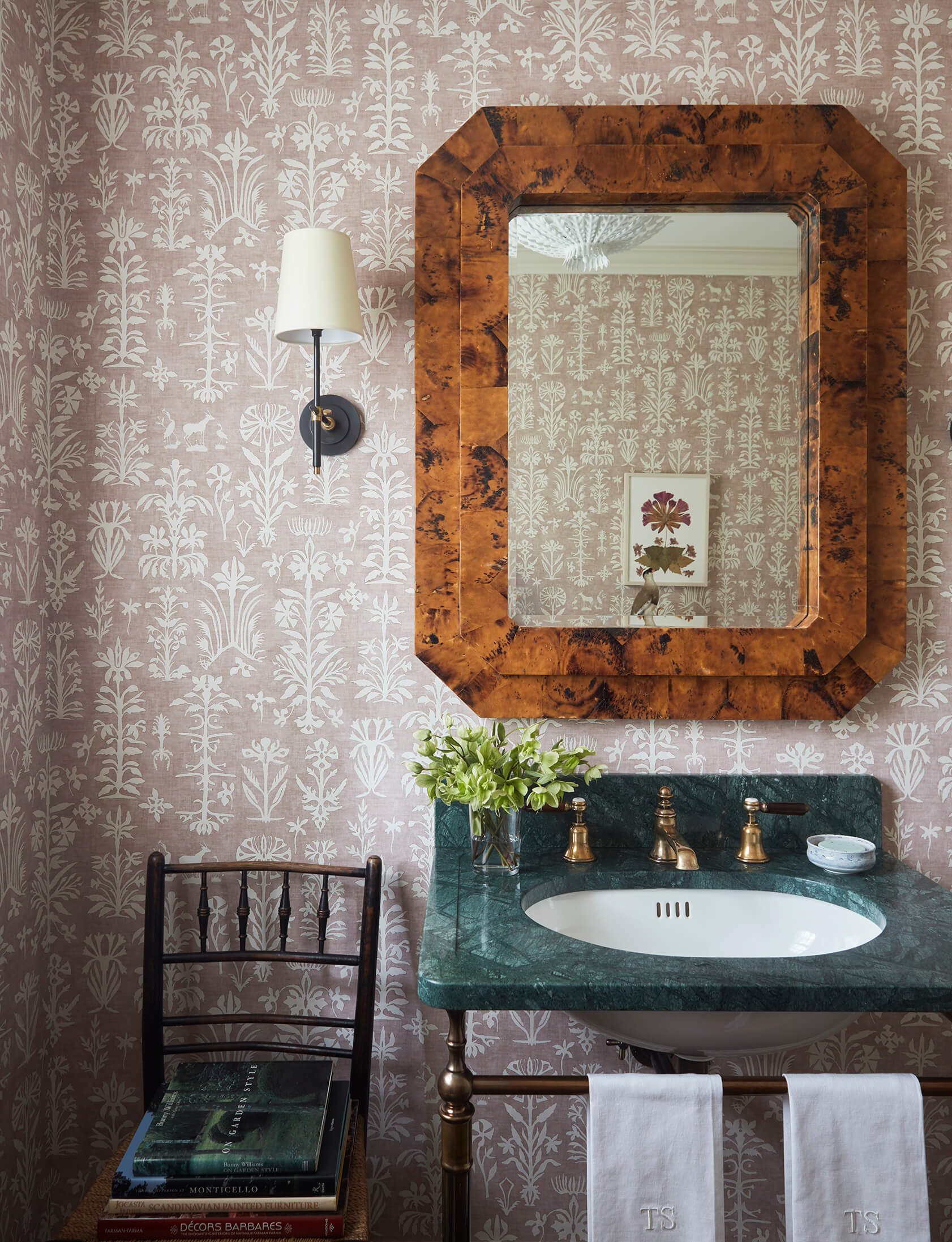 Powder room with dusty rose and white floral patterned wallpaper, burl wood frame, green marble sink, scone and chair.