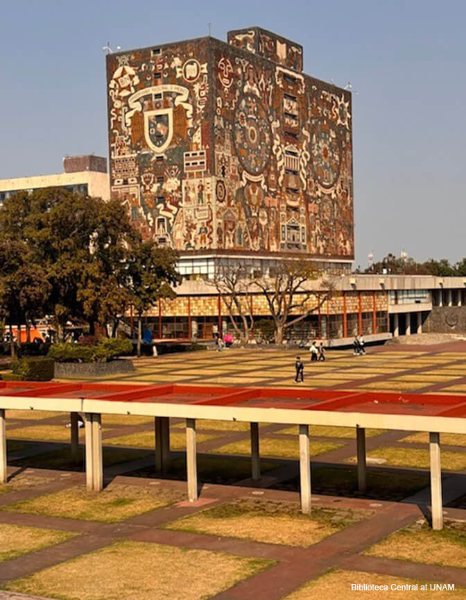 A blue sky with a large block-like building covered in a stone mosaic mural in the distance.
