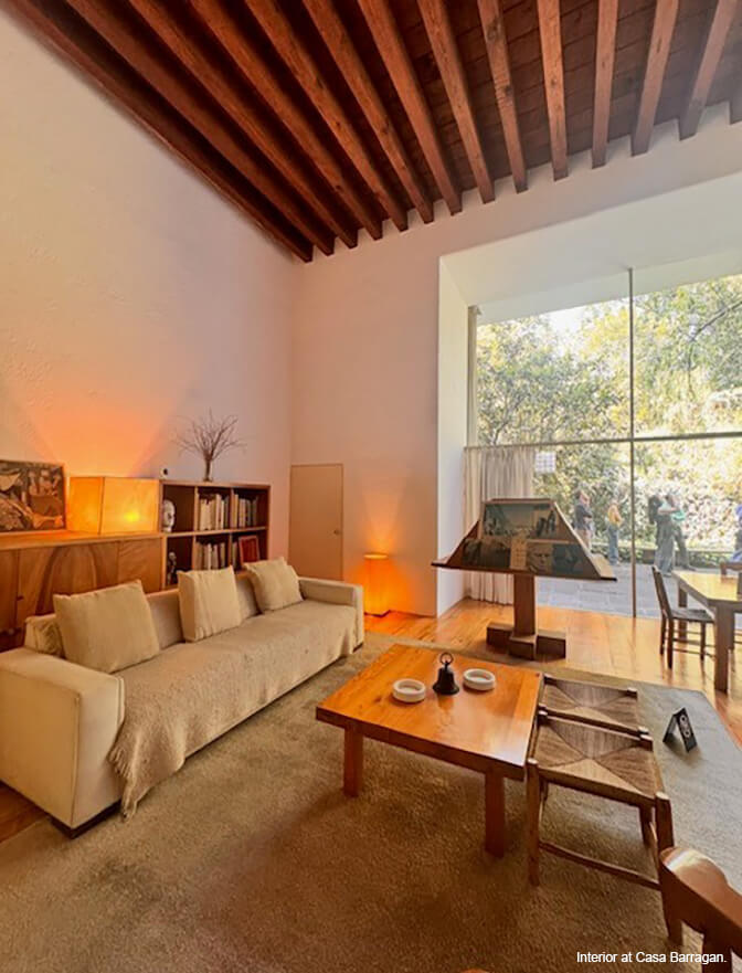 A white-walled living room with wood ceiling, a glass window wall, neutral rug and sofa and wood table.