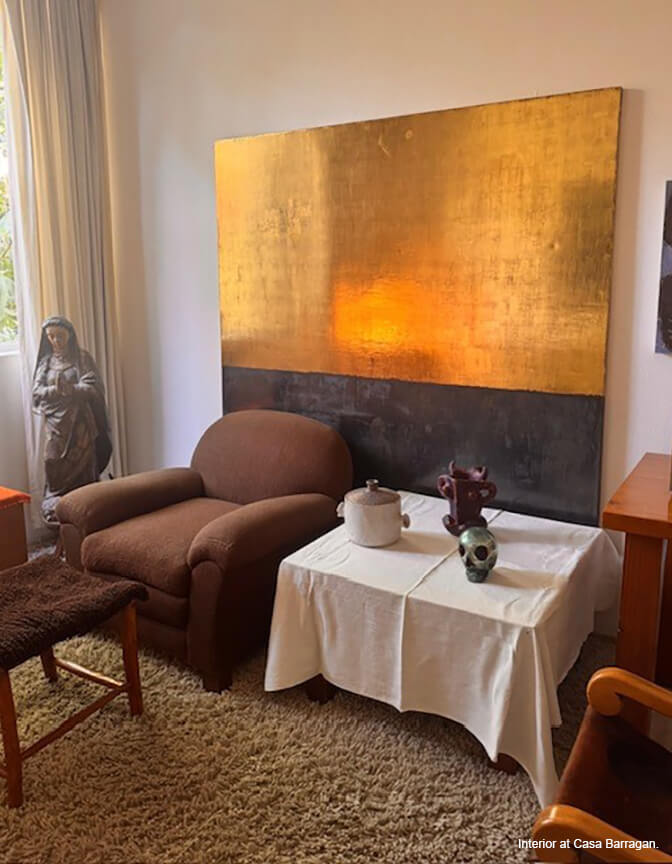 An interior with a large gold and black painting against the wall, a brown upholstered chair and a small table.