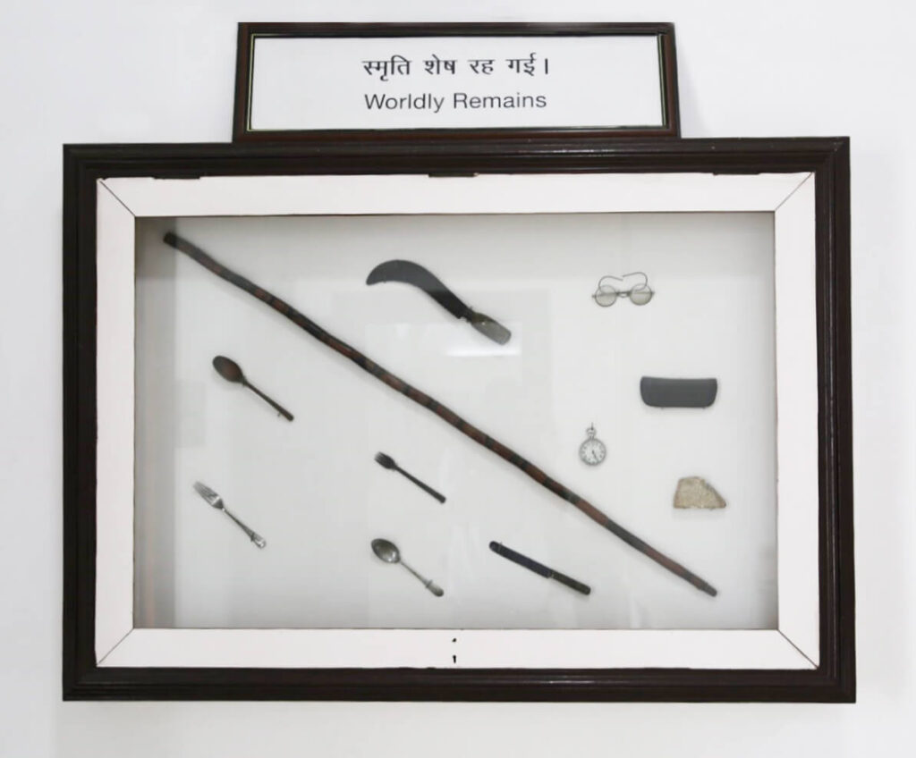 A collection of objects that belonged to Mahatma Gandhi, in a black picture frame with the title “Worldly Remains.”