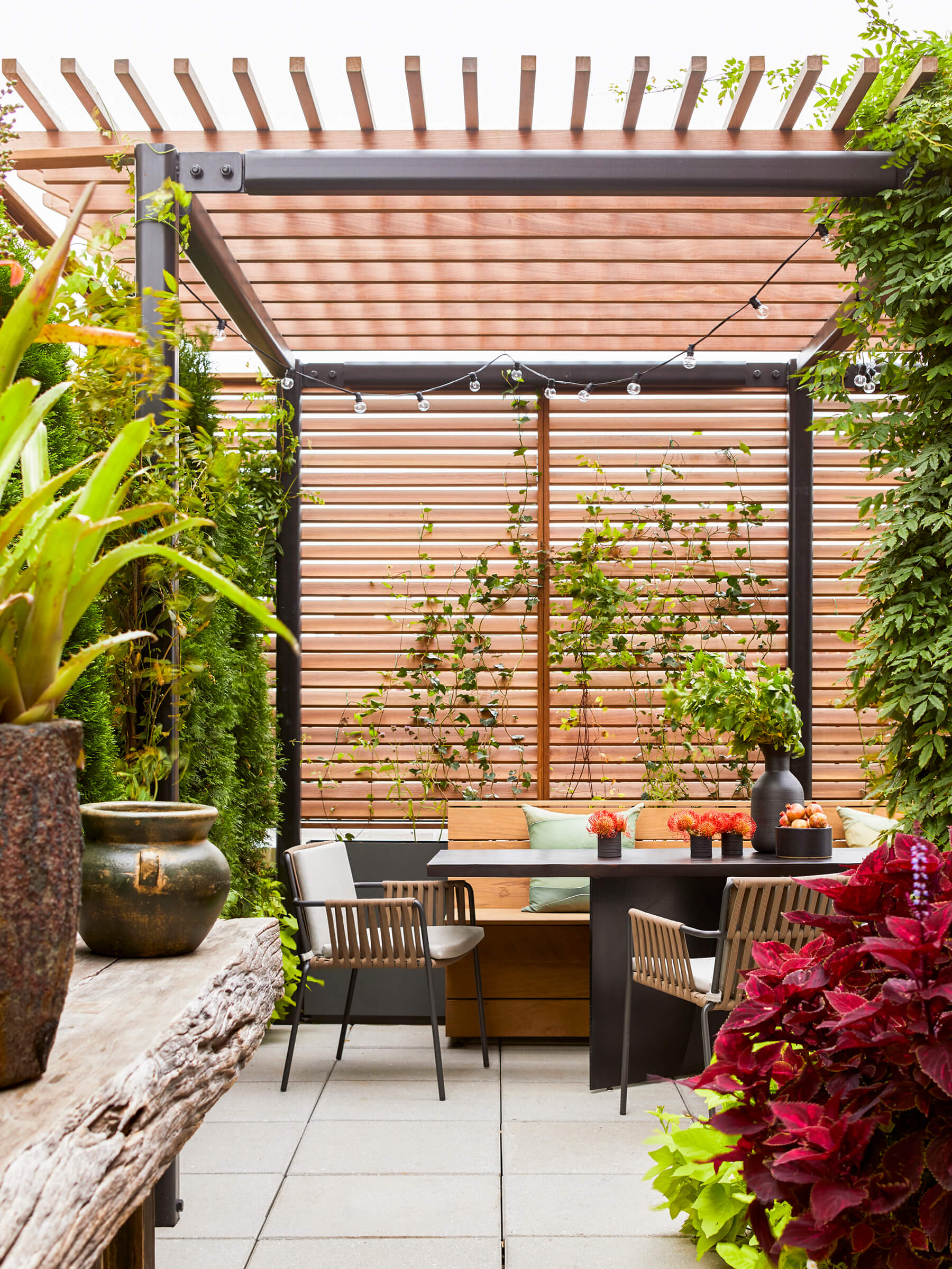 A terrace with a dining table and chairs situated inside a wood slat enclosure with plantings.