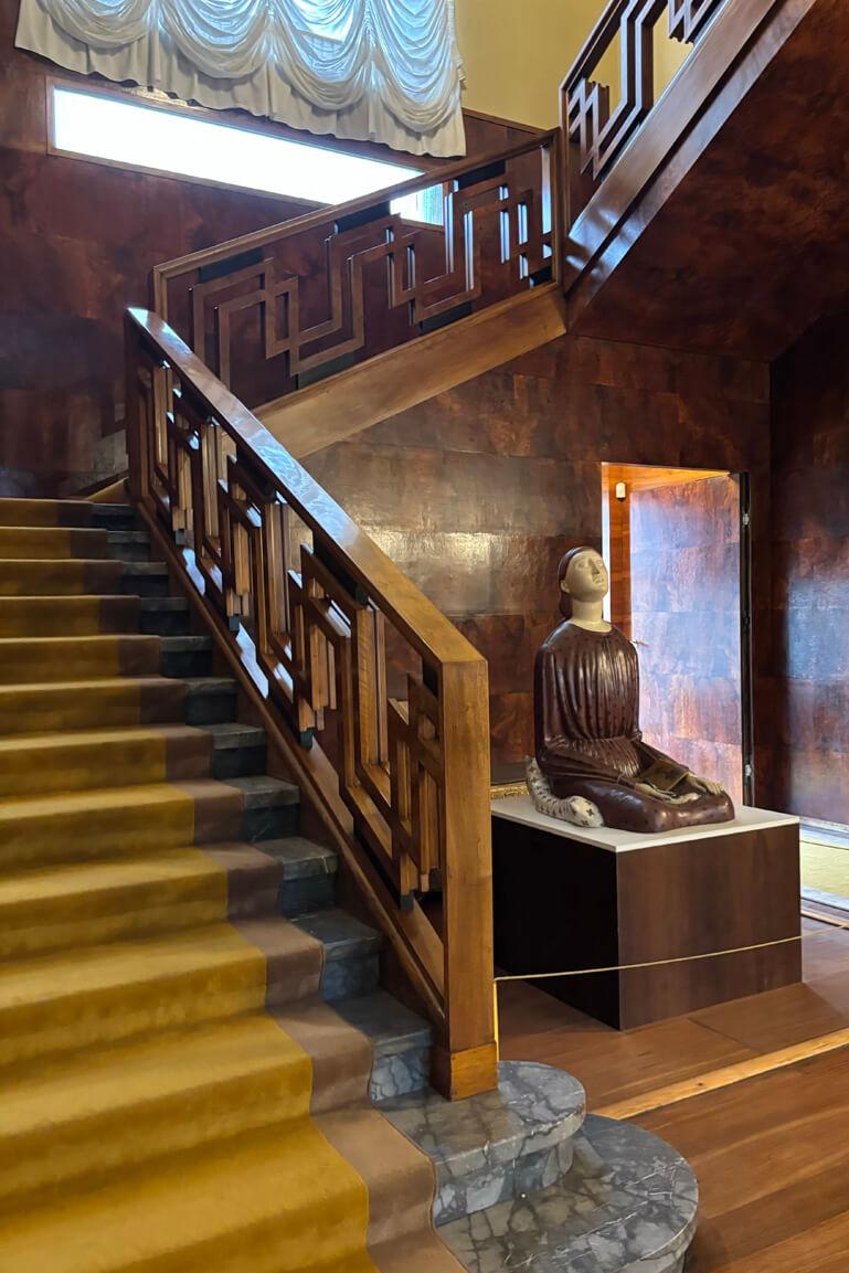 Carpet-lined stone staircase with geometric wood banister and wood tiled walls at the entry at Villa Necchi Campiglio in Milan.
