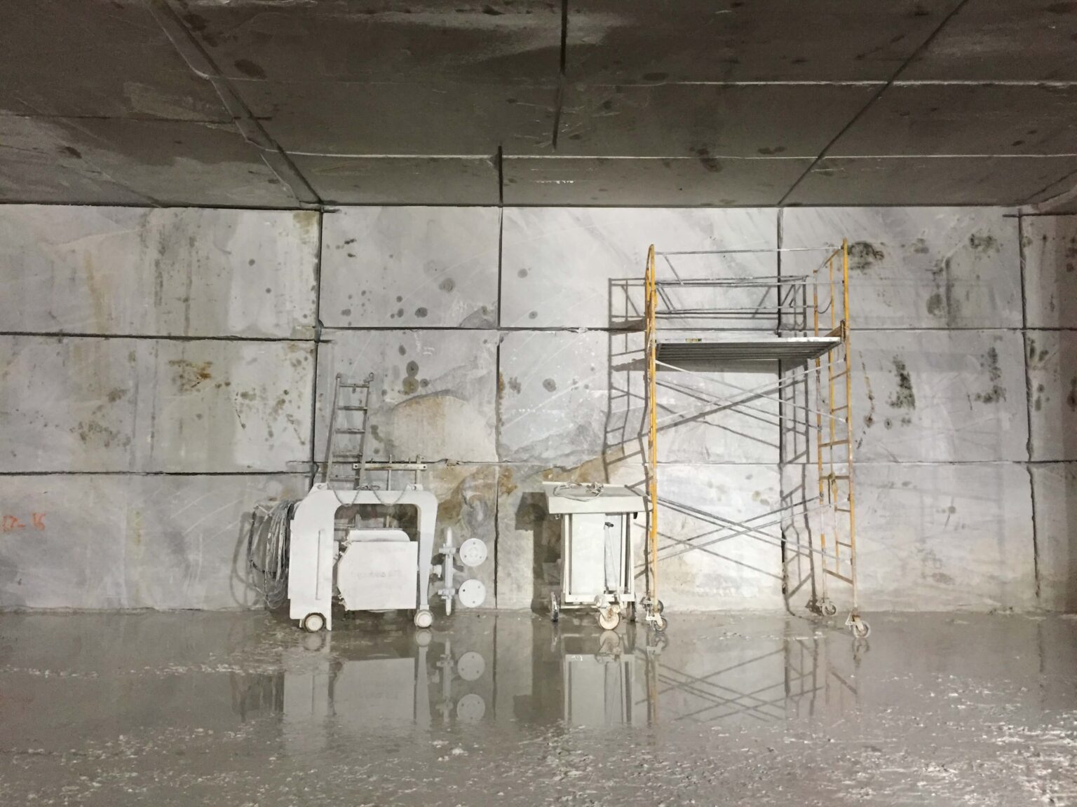 Interior of a marble quarry with marble ceiling and back wall, with machinery and a rolling cart and a white mud floor.