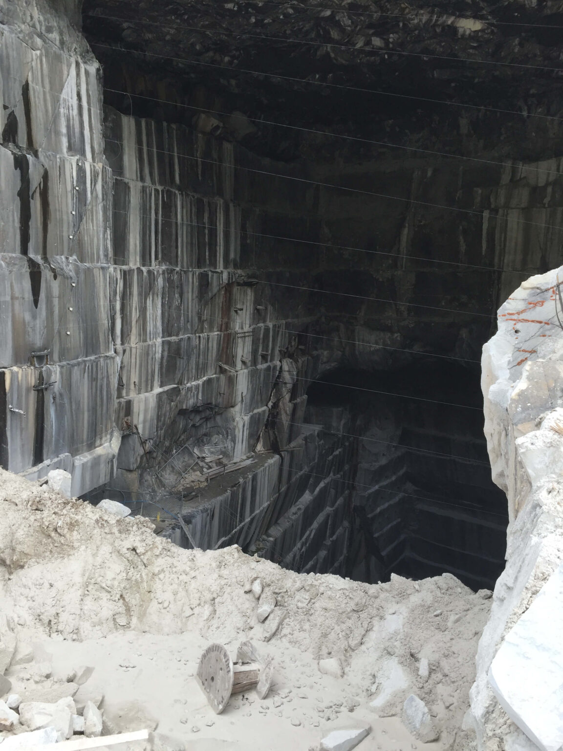 View inside a quarry showing dark gray stone; white dirt and rocks in the foreground.