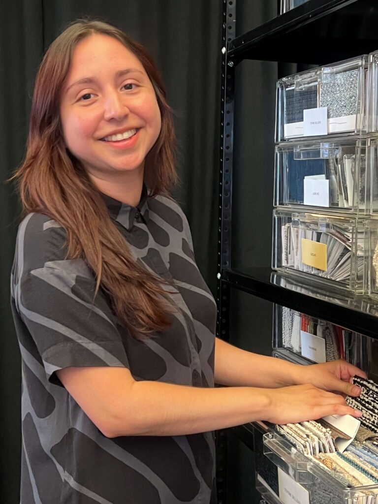 A woman with brown hair standing with her hands in a draw of fabric samples in a design office.