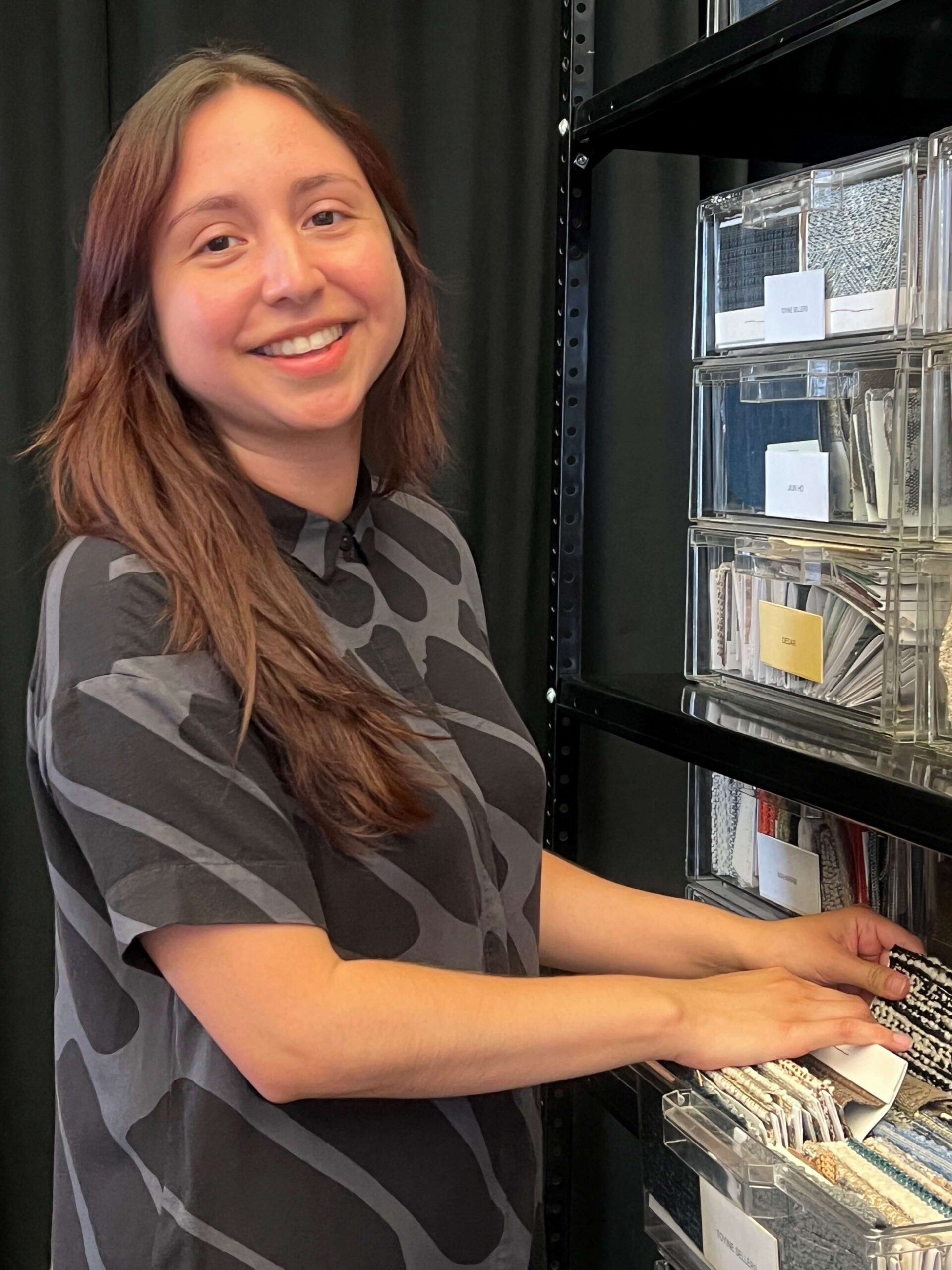 A woman with brown hair standing with her hands in a draw of fabric samples in a design office.
