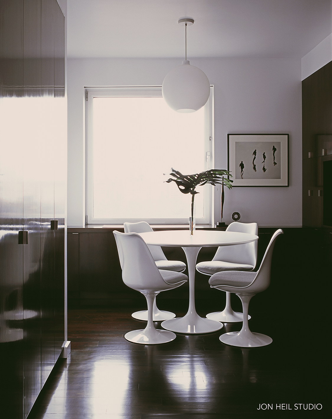 Breakfast room with white walls and dark wood floor with a white Tulip table and chairs and a white spherical pendant light.