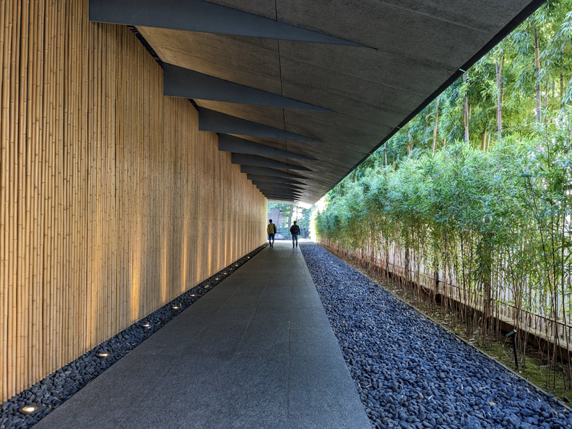 A covered walkway with a wooden wall to the left and a wall of bamboo and pebbles to the right. 