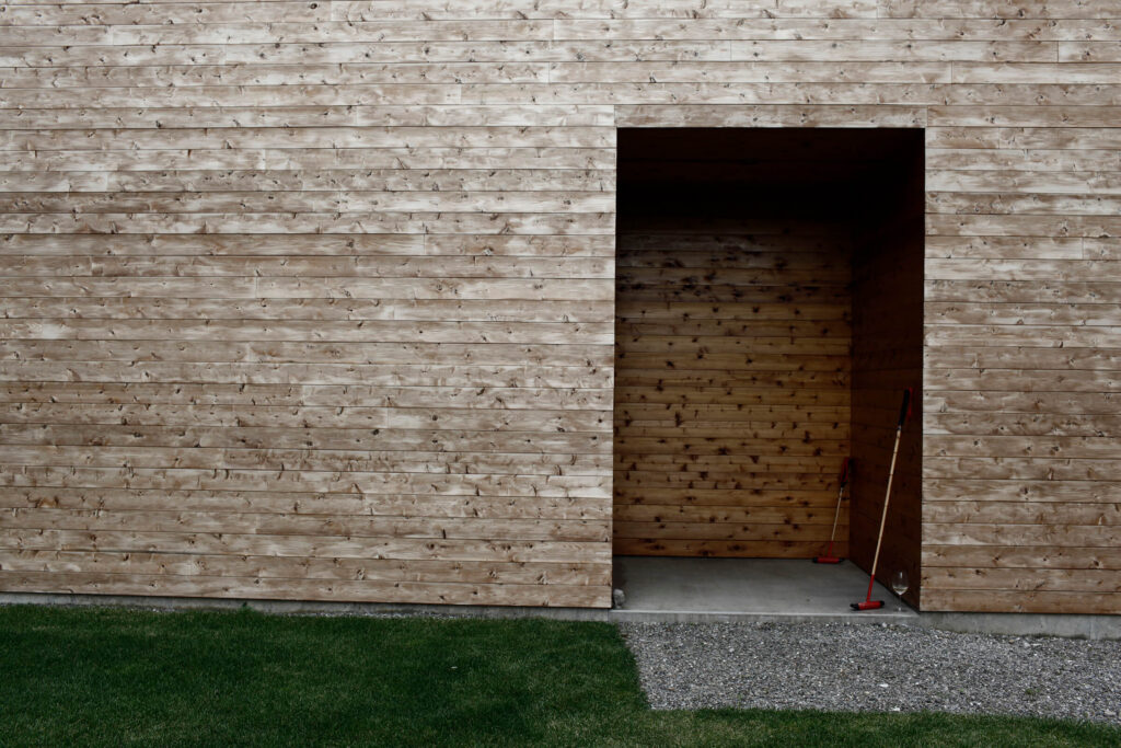 A close-up of a modern house clad in cedar shingles with a cut-out doorway and grass in the foreground.