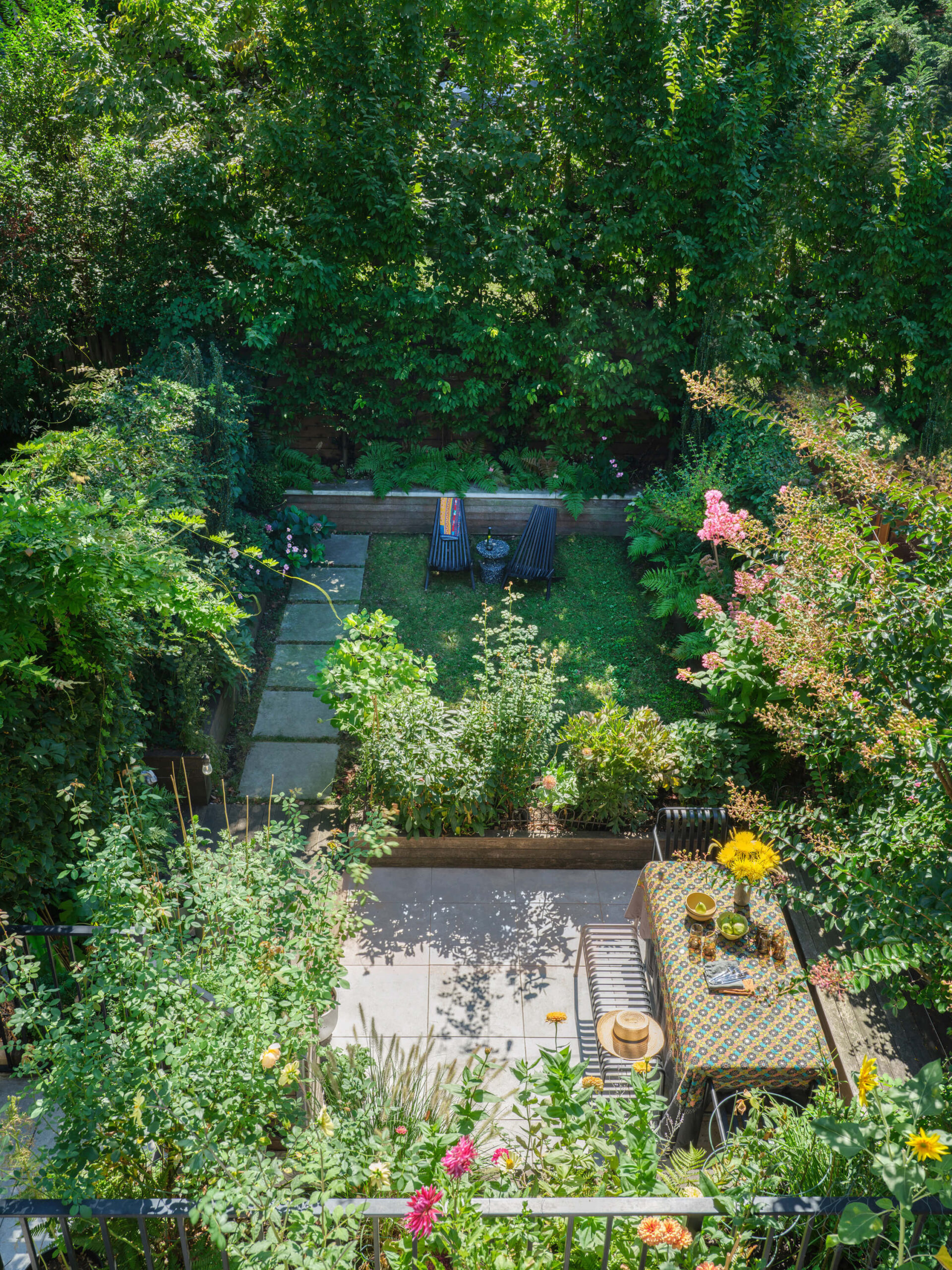 Townhouse back patio with bench and dining table and footpath to grassed garden with shrubs and flowers in full bloom.