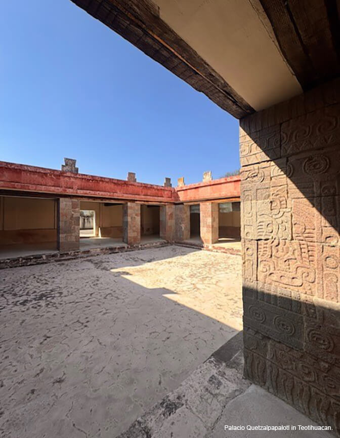 A low building with stone columns and a red-colored flat roof surrounding an open courtyard with a bright blue sky.