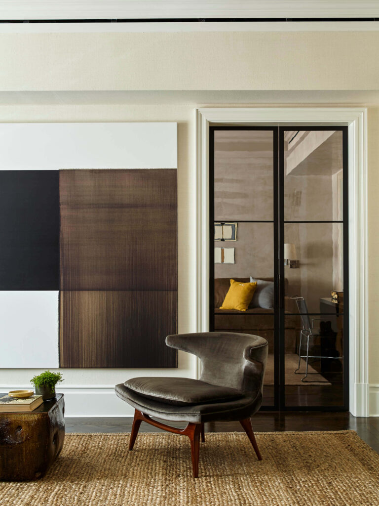 Residential interior with white walls, natural fiber rug, brown and black artwork, interior glass door and chair.